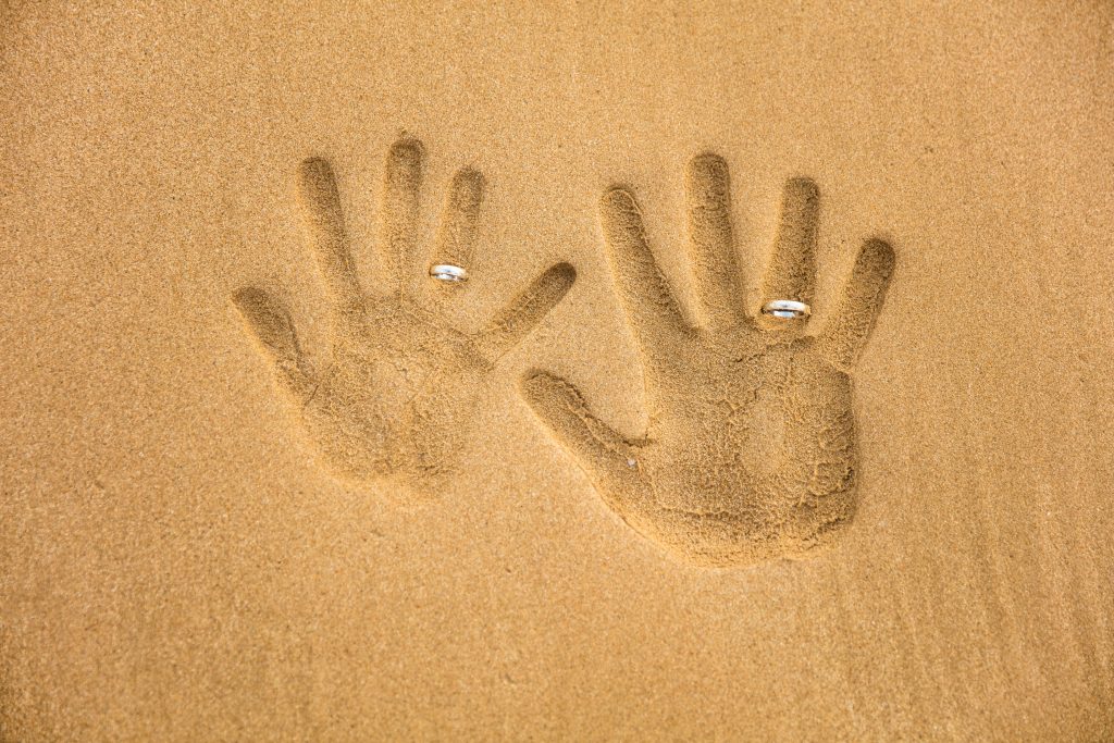 Hand prints in the sand with wedding rings