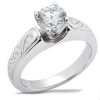 A silver ring with a large round diamond sits prominently atop an intricately engraved band.