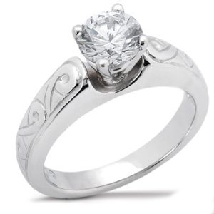 A silver ring with a large round diamond sits prominently atop an intricately engraved band.