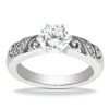 A silver engagement ring features a large round diamond at the center with intricate detailing on the band.