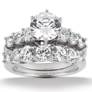 A diamond engagement ring set features a central round-cut diamond surrounded by smaller round diamonds on a white metal band.