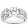 A silver engagement ring features a central round diamond flanked by two smaller diamonds on either side, with additional smaller stones set in the band.
