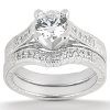 A silver engagement ring set features a prominent round diamond at the center with ornate detailing on the bands.