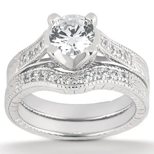A silver engagement ring set features a prominent round diamond at the center with ornate detailing on the bands.
