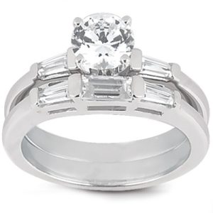 A silver engagement ring features a large round diamond center stone flanked by two rows of rectangular diamonds.