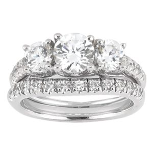 A silver engagement ring features three large round diamonds and a band adorned with smaller diamonds.