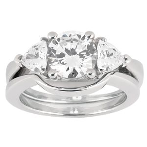 Three-stone engagement ring featuring a central round diamond flanked by two smaller round diamonds, set in a polished white metal band.