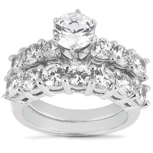 A silver ring features a central round diamond surrounded by smaller diamonds arranged in a floral pattern.