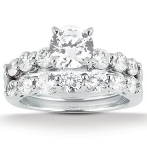 A silver ring set features a central round diamond surrounded by smaller diamonds on a curved band.