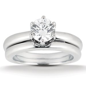 A silver-colored engagement ring with a round diamond setting sits atop a matching wedding band.