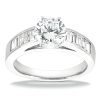 A diamond engagement ring with a round center stone and rectangular side stones is displayed on a smooth surface.