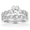 A white gold engagement ring set features a central round diamond surrounded by smaller pave-set diamonds in a twisted band design.