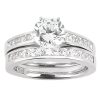 A silver engagement ring set features a central round diamond surrounded by smaller rectangular stones on the band.