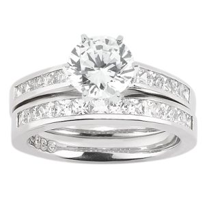 A silver engagement ring set features a central round diamond surrounded by smaller rectangular stones on the band.