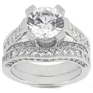 A silver engagement ring features a large round diamond centerpiece surrounded by smaller diamond accents.