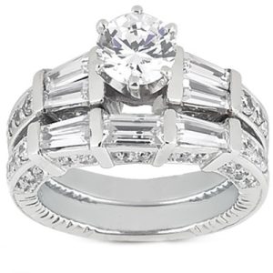 A silver engagement ring features a round center diamond surrounded by rectangular and smaller stones in a layered design.
