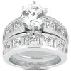 A silver engagement ring set showcases a sparkling round diamond at the center, surrounded by smaller rectangular and square-cut stones along the band.