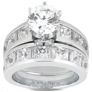 A silver engagement ring set showcases a sparkling round diamond at the center, surrounded by smaller rectangular and square-cut stones along the band.