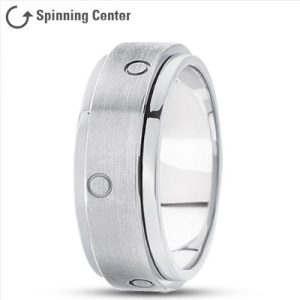 A metallic ring with a brushed finish and circular indentations is displayed against a plain background.