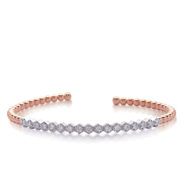A metal cuff bracelet features alternating rose gold spheres and a row of hexagonal diamond-like embellishments.