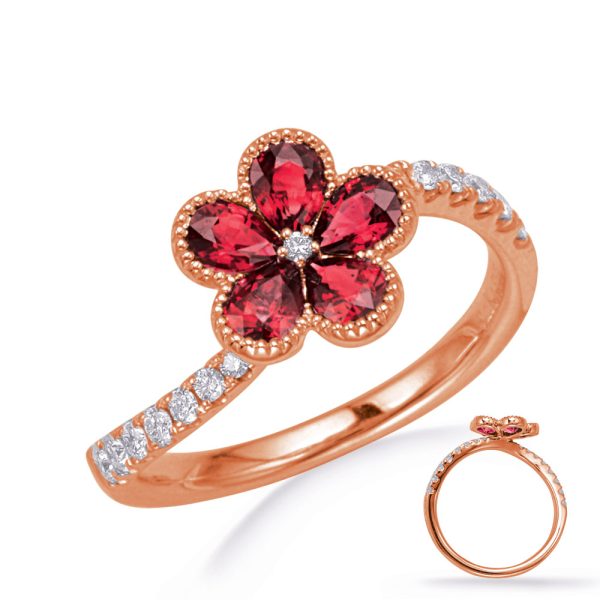 A rose gold ring features a flower design with red gemstones at the center, surrounded by clear stones along the band.