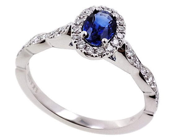 A silver ring is displayed with an oval blue gemstone at the center, surrounded by small clear stones.