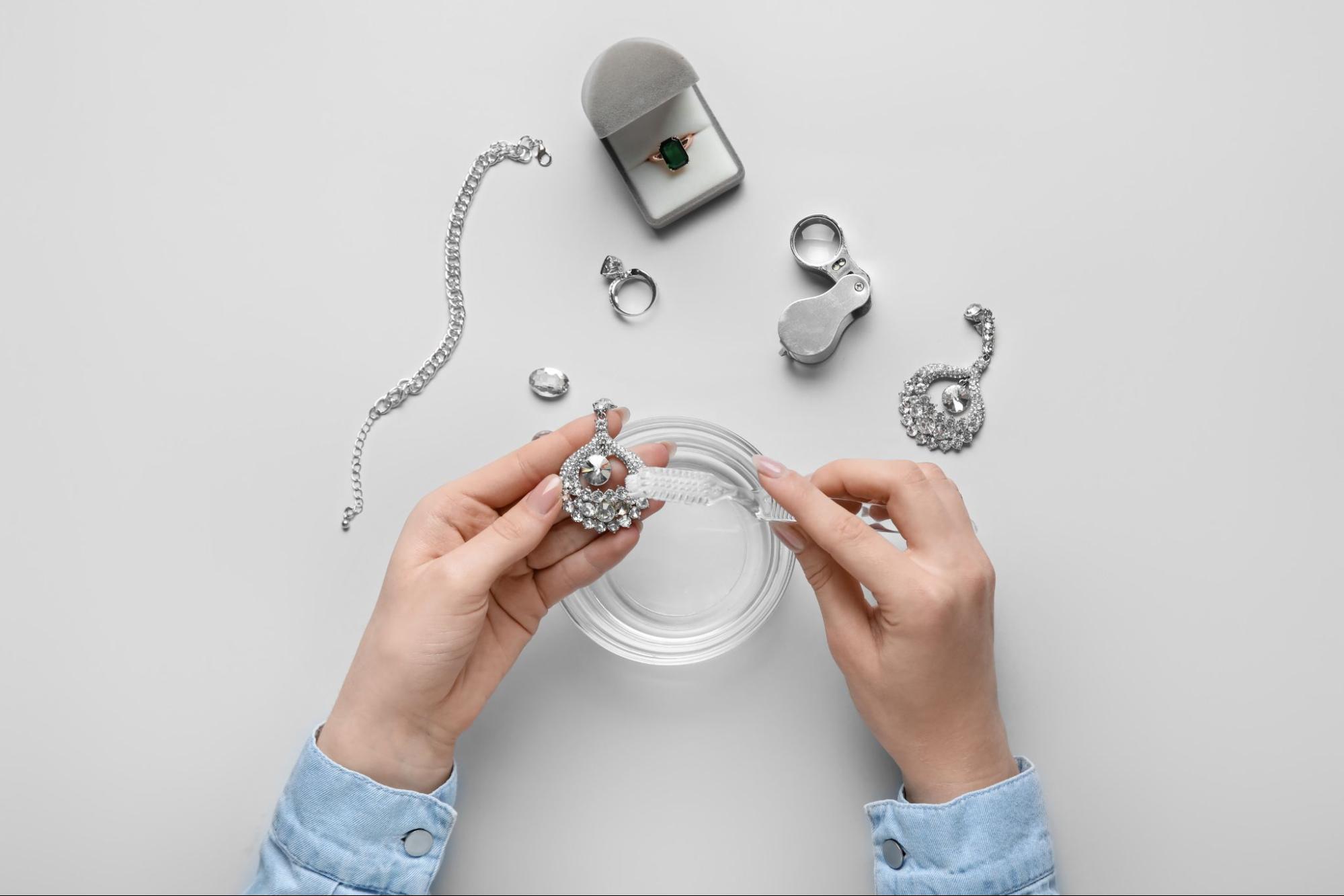 A person cleaning their jewelry with a brush over a bowl of water