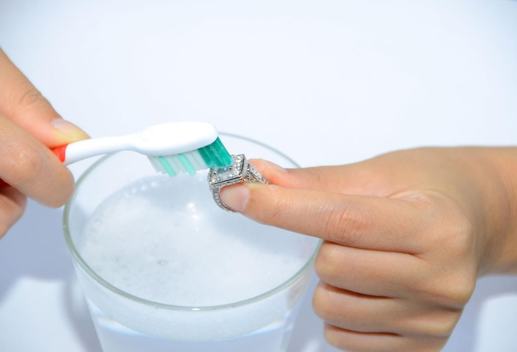 A person cleaning their diamond ring with a toothbrush 